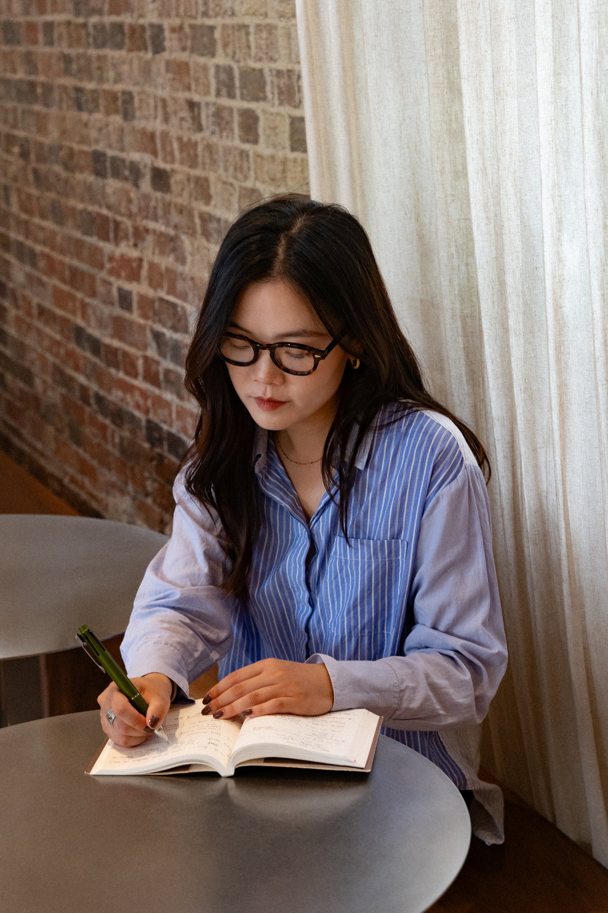 Nina Xu writing in a notebook at a cafe table against a brick wall