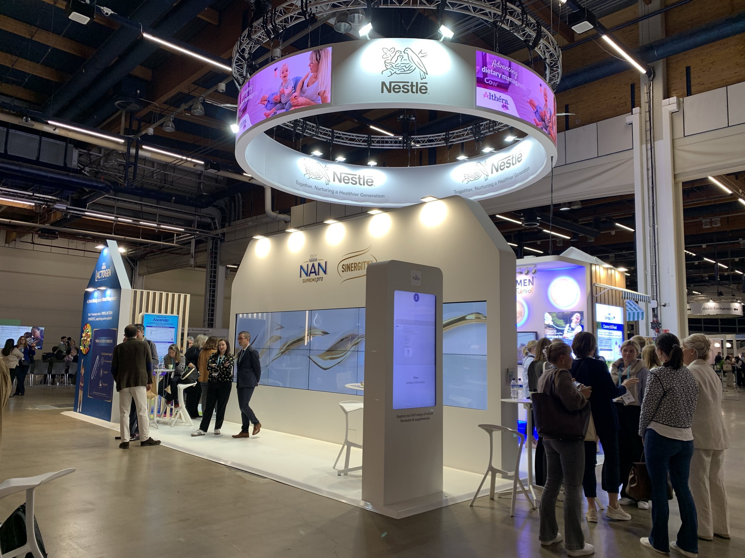 Nestlé stand at ESPGHAN 2025: the illuminated Nestlé ring above the NAN Supreme Pro and Sinergity structure, its screen wall and interactive product kiosk